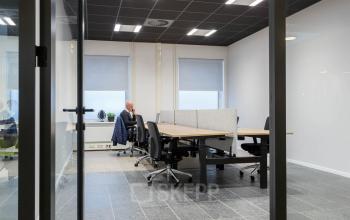 Binnenzicht van een kantoorpand op Stadhuisplein 10, Eindhoven Centrum, met werkplekken en een persoon in zakelijk overleg. Ideale locatie voor kantoorruimte huren.