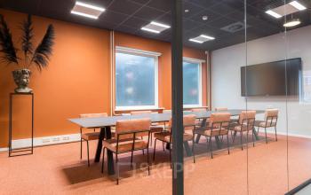 Moderne vergaderruimte met oranje muren en lederen stoelen in een kantoorpand op Stadhuisplein 10, Eindhoven Centrum. De ruimte is geschikt voor zakelijke bijeenkomsten en biedt comfortabele zitplaatsen met natuurlijke lichtinval.