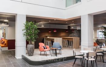 Moderne kantoorruimte met zitgedeelte op Stadhuisplein 10, Eindhoven Centrum. Verschillende stoelen en tafels creëren een gezellige sfeer voor zakelijke ontmoetingen of pauzes. Groene planten brengen een natuurlijke touch in de inrichting.