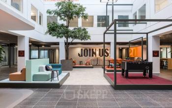 Modern ingerichte lounge in kantoor op Stadhuisplein 10, Eindhoven Centrum met zitgedeelten, een tafelvoetbaltafel en groene accenten voor huur. Kantoorruimte geschikt voor ontspannen werkoverleg.