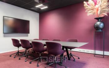 Kantoorruimte huren bij Stadhuisplein 10 in Eindhoven Centrum met een moderne vergaderruimte. Donkerrode muren, een grote tafel met bijpassende stoelen en een flatscreen zorgen voor een professionele sfeer.