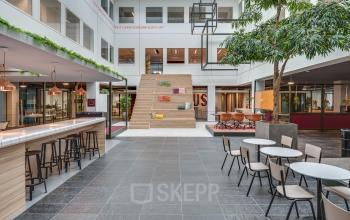 Moderne kantoorruimte te huur op Stadhuisplein 10, Eindhoven Centrum. De open ruimte heeft een mix van zitplekken en een grote trap met kussens. Geschikt voor diverse zakelijke activiteiten.