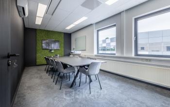 Vergaderruimte met lange tafel, omringd door stoelen, een scherm aan de muur en ramen die het kantoorpand lichte uitstraling geven aan Meerenakkerplein 1-10 in Eindhoven De Hurk.