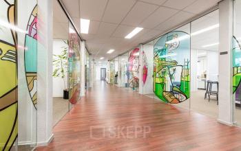 Kleurrijk kantoorpand op Meerenakkerplein 11-20 in Eindhoven De Hurk, met glaspanelen met kunstwerken langs de gang. Ideaal voor wie kantoorruimte wil huren met een inspirerende uitstraling.