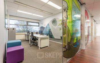 Kantoorruimte te huur op Meerenakkerplein 11-20, Eindhoven De Hurk. Licht interieur met glazen wanden, kleurrijke muurtekeningen, bureau en stoelen. Geschikt als werkruimte.