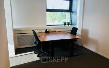 Ingericht kantoor gelegen aan Hurksestraat 60, Eindhoven De Hurk met twee bureau’s, stoelen en een raam met uitzicht, ideaal voor kantoorruimte huren.
