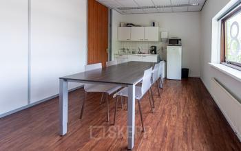 Kantoorruimte huren in Eindhoven Noord, Le Havre 114-127. Helder interieur met grote ramen, donkere houten vloer, tafel en stoelen, kitchenette met koelkast en magnetron.
