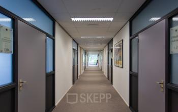 Een lange gang in een kantoorpand op Weegschaalstraat 3 in Eindhoven Noord, zonder aanwezige personen, met neutrale muren en deuren aan beide zijden.