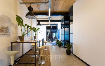 Moderne kantoorruimte te huur aan de Weegschaalstraat 3 in Eindhoven Noord, met hoge plafonds, industriële lampen en planten voor een frisse uitstraling.