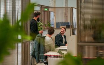 Kantoorruimte huren in Eindhoven Strijp-S met gezellig ingerichte werkplekken waar drie personen samenwerken en overleggen, met natuurlijke elementen in de omgeving.