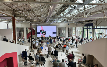 Interieur van een hip kantoorgebouw op Frederiklaan 10A, Eindhoven Strijp-S met een grote groep mensen die aan tafels zitten tijdens een presentatie. Geschikt om te gebruiken als inspirerende werkruimte of voor het huren van kantoren.