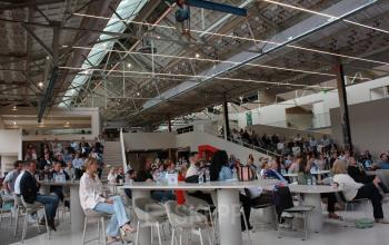 Kantoorpand Frederiklaan 10A in Eindhoven Strijp-S met een grote open ruimte waar mensen in een bijeenkomst zitten. Deze plek biedt een inspirerende omgeving voor zakelijke activiteiten.