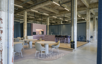 Ruime kantoorruimte huren in een industrieel pand. Moderne inrichting met tafels en stoelen, naast een stijlvolle pantry met balkenplafond op Frederiklaan 10A, Eindhoven Strijp-S.