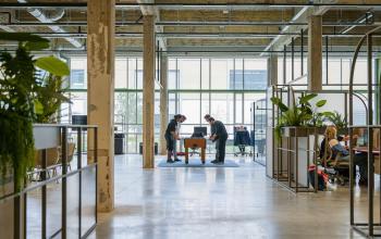 Industriële kantoorruimte huren aan de Frederiklaan 10A in Eindhoven Strijp-S met open vloerplan. Mensen werken en spelen tafelvoetbal in een modern, groen ingerichte setting.