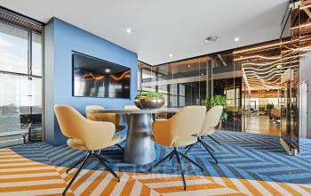 Moderne kantoorruimte met glazen wanden, kleurrijk tapijt en stijlvolle stoelen rond een tafel. Ideaal voor kantoorruimte huren op Achtseweg Zuid 159R in Eindhoven Strijp-S.