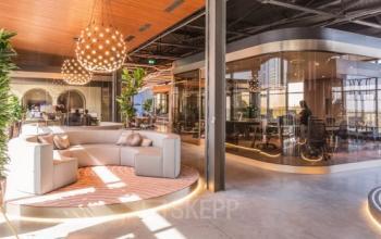 Moderne kantoorruimte huren in kantoorpand op Achtseweg Zuid 159R, Eindhoven Strijp-S, met stijlvolle meubels en grote ramen. Personen werken in een vergaderruimte en open werkplekken.