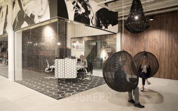 Moderne kantoorruimte huren in Eindhoven Strijp-S op Frederiklaan 10E met glazen wanden, stijlvolle meubels en decoratieve elementen. Personen voeren zakelijke activiteiten uit, zittend in designstoelen.