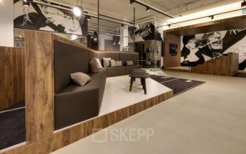 Moderne kantoorruimte met stijlvolle houten en bruine details, comfortabele zitplaatsen en kunstzinnige decoraties op de muren. Een ideale plek voor informele vergaderingen of ontspanning in Eindhoven Strijp-S.