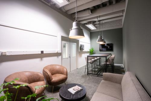 Moderne kantoorruimte huren in Eindhoven Strijp-S met stijlvolle zitplaatsen, hoge tafels en decoratieve planten voor een fris en uitnodigend interieur.