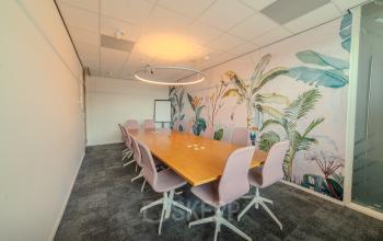 Vergaderruimte met grote houten tafel en zachte stoelen op Torenallee 20, Eindhoven Strijp-S, ideaal voor kantoorruimte huren. Tropische accentmuur biedt een creatieve touch.