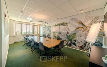 Vergaderruimte met grote houten tafel en acht stoelen op Torenallee 20 in Eindhoven Strijp-S. De muren zijn versierd met een plantenmotief, ideaal voor wie een kantoorpand wil huren.