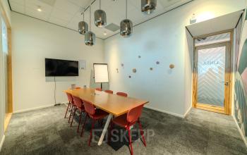 Vergaderruimte met een houten tafel en zes rode stoelen, TV aan de wand en speelse decoratie in een kantoorpand aan Torenallee 20, Eindhoven Strijp-S.