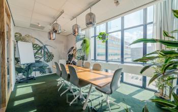 Heldere vergaderruimte op Torenallee 20, Eindhoven Strijp-S, met grote ramen, groene accenten en een lange houten tafel om te huren als kantoorruimte.