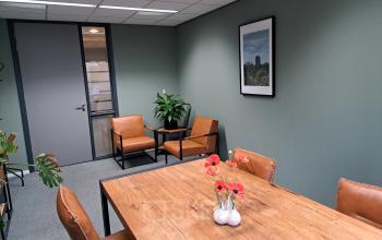 Gezellige kantoorruimte huren aan Hoenderkamp 20 in Emmen met moderne inrichting, houten tafel, leren stoelen en groene accenten. Ideale plek voor bijeenkomsten en vergaderingen.