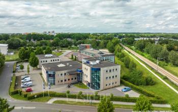 Exterieur van het kantoorpand Hoenderkamp 20 in Emmen, omringd door groene bomen en parkeerruimte. Ideale locatie voor kantoorruimte huren in een rustige omgeving.