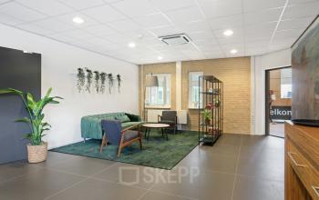 Interieur van een kantoorpand op Hoenderkamp 20 in Emmen met een uitnodigende ontvangstruimte, groene bank, houten stoelen en een plantenrek. Ideale locatie om kantoorruimte te huren.