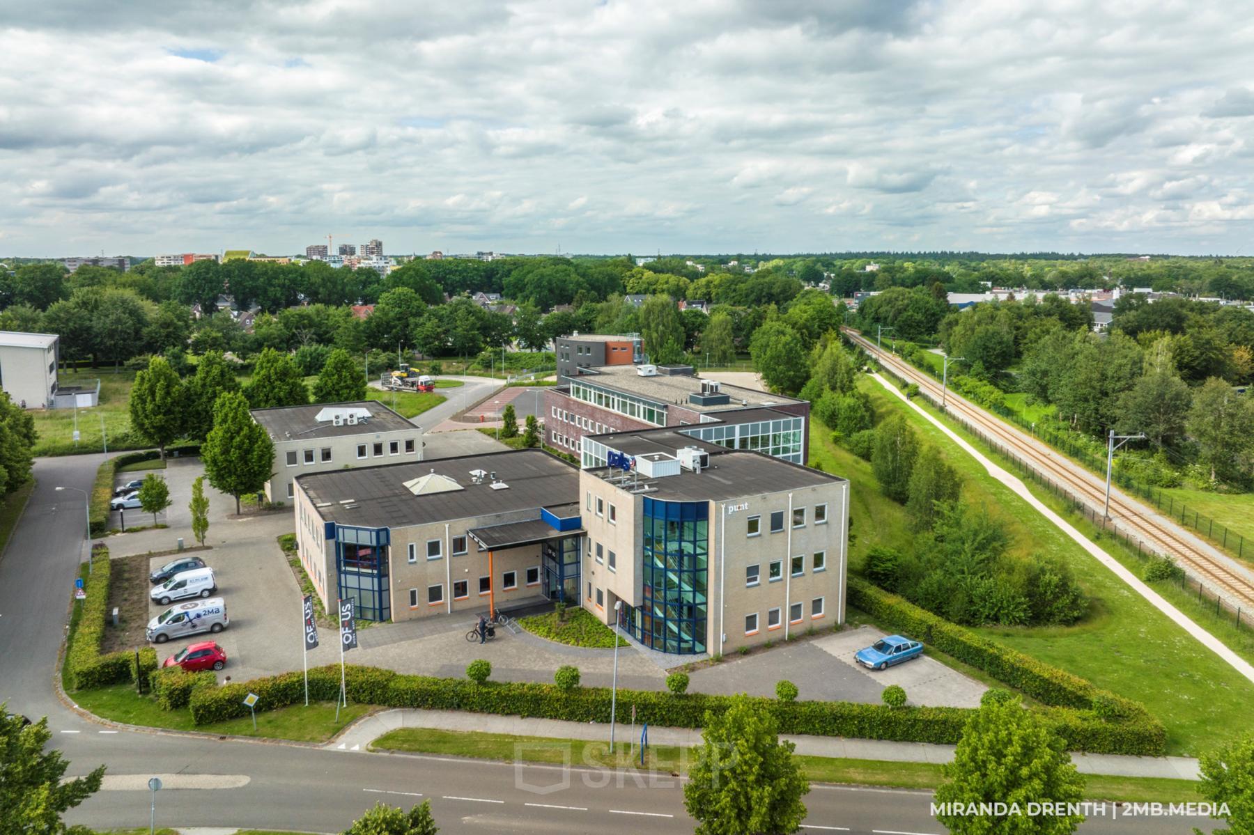 Exterieur van het kantoorpand Hoenderkamp 20 in Emmen, omringd door groene bomen en parkeerruimte. Ideale locatie voor kantoorruimte huren in een rustige omgeving.