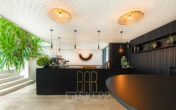 Moderne kantoor bar op Brouwerijstraat 1 in Enschede met stijlvolle verlichtingsarmaturen en een groot aanrecht. Aantrekkelijke ruimte voor informele ontmoetingen en sociale activiteiten binnen het kantoorpand.