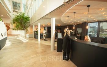 Kantoorpand aan Brouwerijstraat 1 in Enschede met moderne inrichting. Twee personen zijn in gesprek aan een receptiebalie.