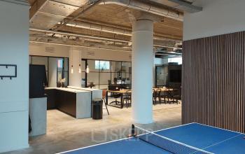 Kantoorruimte huren in Enschede met open indeling, moderne werkplekken en speelse voorzieningen. De ruimte is industrieel ingericht met tafels en stoelen, geschikt voor diverse werkactiviteiten.