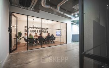 Kantoorruimte huren op Brouwerijstraat 1 in Enschede. Mensen in een moderne vergaderruimte met glazen wanden, bezig met een zakelijke bespreking.