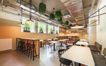 Kantoorruimte huren op Brouwerijstraat 1, Enschede: Moderne ruimte met tafels, stoelen, hangplanten en grote ramen.