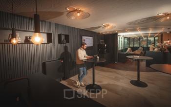 Gezellige en moderne kantoorruimte op Brouwerijstraat 1 in Enschede met sfeerverlichting, hoge tafels en enkele mensen bezig met laptopwerk, ideaal voor kantoorruimte huren.