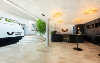 Moderne receptie van een kantoorpand aan Brouwerijstraat 1, Enschede, met stijlvolle verlichting en een ronde trap. Ideaal voor wie kantoorruimte wil huren in een representatief gebouw.