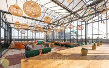 Moderne kantoorruimte huren op Brouwerijstraat 1, Enschede. Ruime open werkruimte met veel licht, houten tafels, groene stoelen en hanglampen.