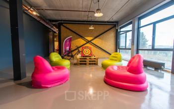 Modern ingerichte loungehoek in kantoorpand op Marssteden 52-54 in Enschede met kleurrijke zitzakken en een dartbord.