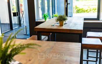 Moderne kantoorruimte in Enschede met houten tafels en hoge krukken bij grote ramen, voor een inspirerende werkplek in het kantoorpand op Marssteden 20. Ideaal voor kantoorruimte huren.