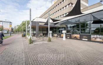 Vooraanzicht van kantoorpand aan de Wethouder Beversstraat 185 in Enschede, geschikt voor kantoorruimte huren, met moderne glazen gevel en buitenzitjes. Gelegen aan een rustige straat, ideaal voor zakelijke activiteiten.