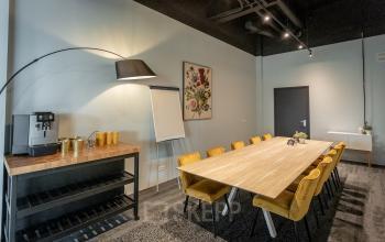 Vergaderruimte in kantoorpand Wethouder Beversstraat 185, Enschede, met lange houten tafel, gele stoelen en espressomachine. Ideale plek voor productieve vergaderingen in moderne kantooromgeving.