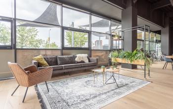 Moderne kantoorlounge in Enschede met grote ramen, stijlvolle meubels, en veel natuurlijke lichtinval. Ideaal om klanten te ontvangen of informeel te vergaderen. Kantoorruimte huren in aantrekkelijk ontwerp.