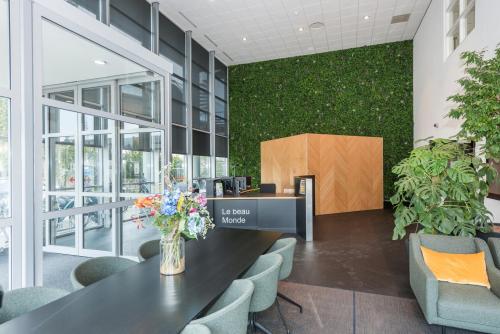 Moderne kantoorpandlobby op Brandweerstraat 20-30 in Enschede met groene muur, receptiebalie, comfortabele stoelen, en een lange tafel met bloemen. Perfecte ruimte voor dynamische zakelijke ontmoetingen.