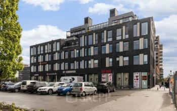 Modern zwart kantoorpand Brouwerijstraat 10 in Enschede met geparkeerde auto's op de voorgrond. Verschillende winkels op de begane grond.