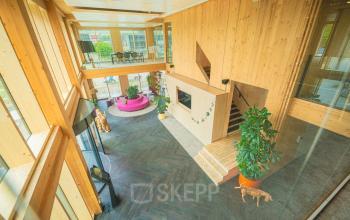 Ruime, houten entree van een kantoorpand aan de Moutlaan 1-23 in Enschede, waarin een moderne en uitnodigende sfeer heerst.
