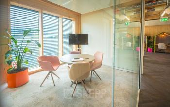 Moderne en lichte kantoorruimte in Enschede op Moutlaan 1-23 met een ronde tafel en comfortabele stoelen, ideaal voor vergaderingen. Grote ramen zorgen voor veel natuurlijk licht.