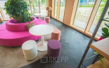 Moderne kantoorruimte met kleurrijke zitgelegenheid en veel natuurlijk licht op Moutlaan 1-23 in Enschede, perfect om te huren. Planten en houten decor zorgen voor een uitnodigende sfeer.