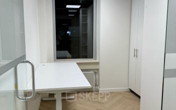 Kantoorruimte huren in Enschede op Hoedemakerplein 2. Smalle kamer met een wit bureau, modern laminaat en een glazen deur. Heldere verlichting maakt het geschikt voor geconcentreerd werk.